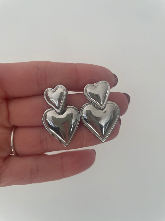Gros plan petites boucles d’oreilles double coeur argent acier inox fond blanc