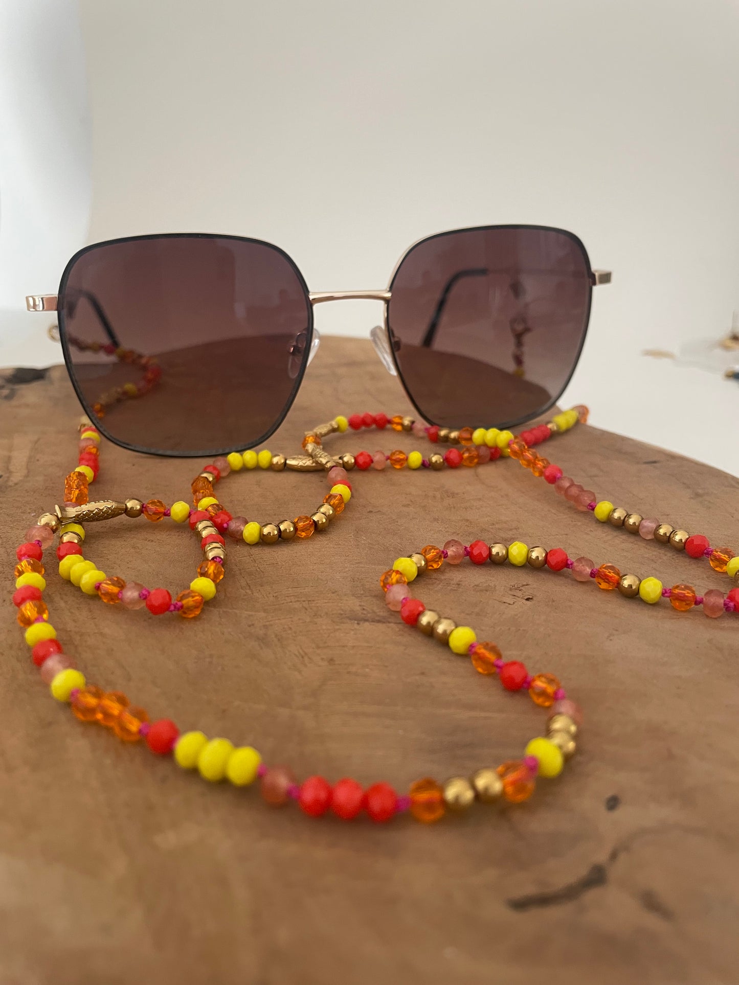 Version chaîne pour lunettes du collier sautoir Jacqueline tons rouge orange jaune et doré, porté sur lunettes de soleil